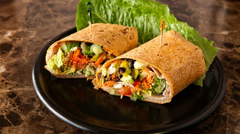 Two colorful wraps filled with fresh vegetables and meat, served on a black plate.