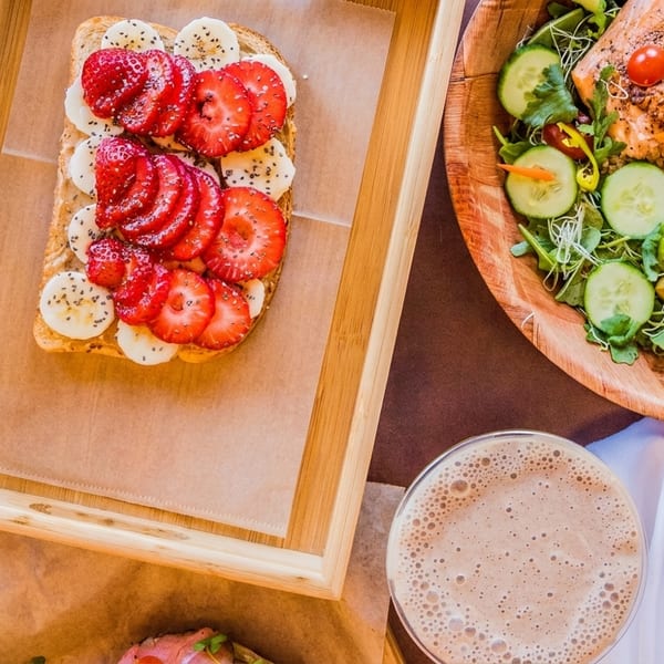 Overhead view of strawberry banana toast, salmon salad, green smoothie, and a chocolate drink.