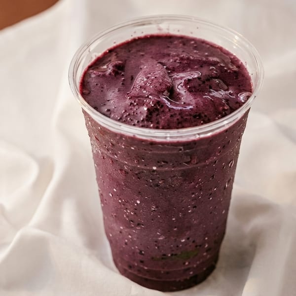 A vibrant purple berry smoothie in a clear plastic cup, condensation visible on the outside.