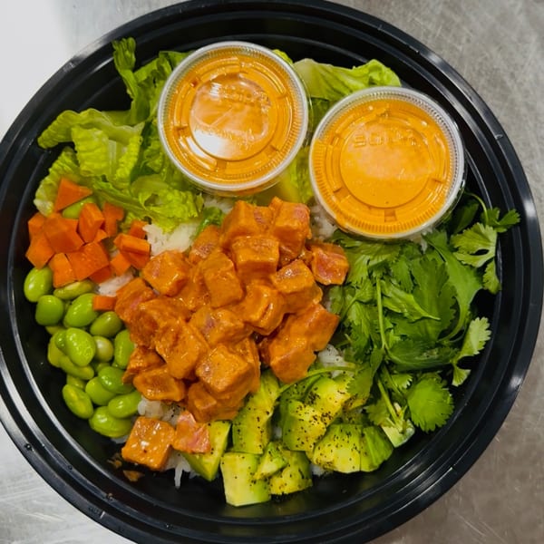A poke bowl with salmon, avocado, edamame, carrots, cilantro, and two sauce cups.
