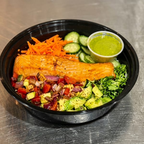 Salmon bowl with avocado, salsa, carrots, cucumbers, cilantro, and green dressing on a metal surface.